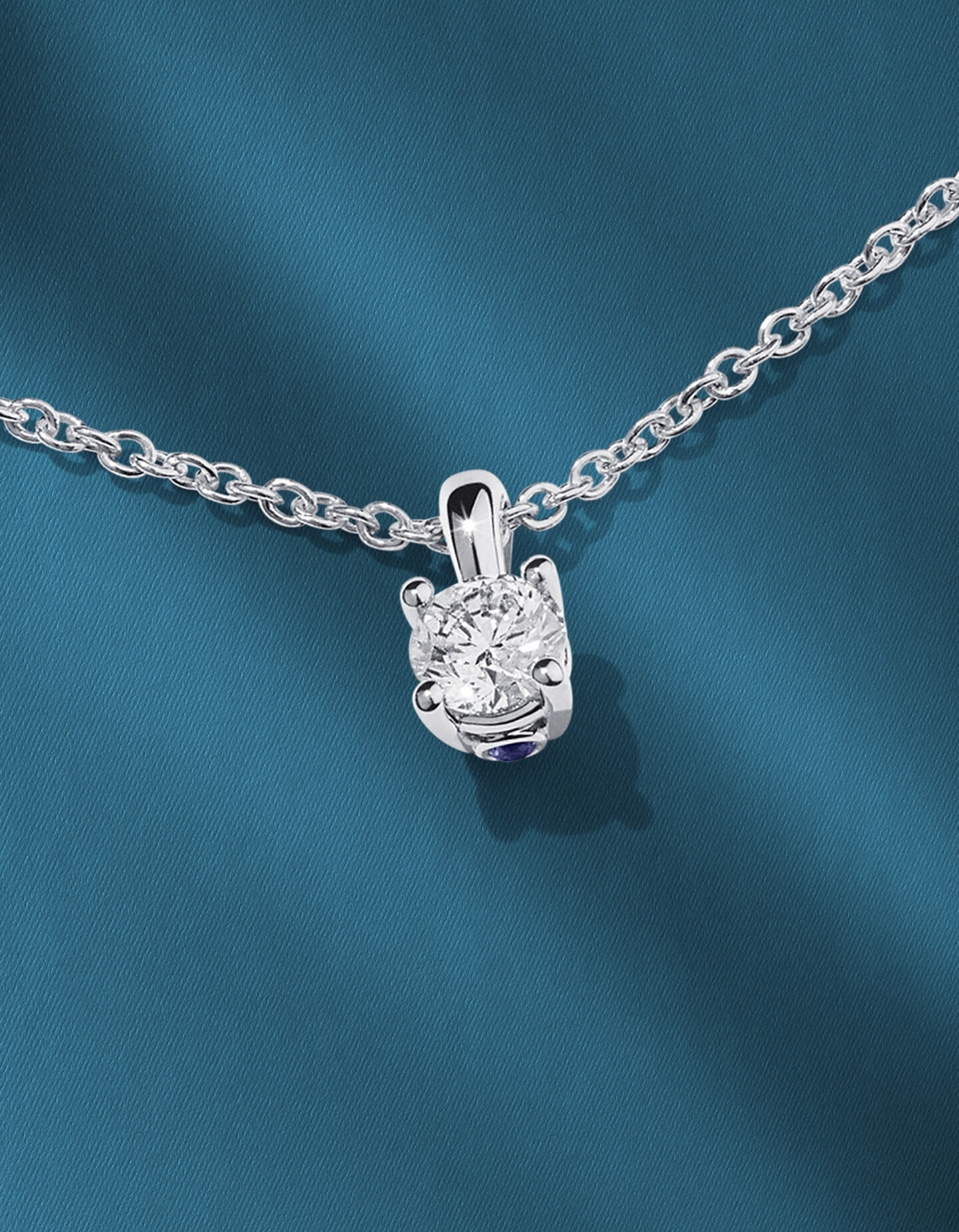 Birks diamond solitaire pendant on a blue background.